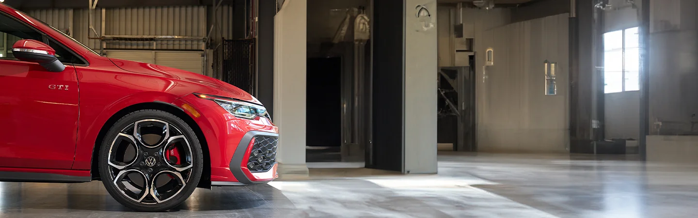 Close up side view of the front end a red 2025 Volkswagen Golf GTI in a wherehouse