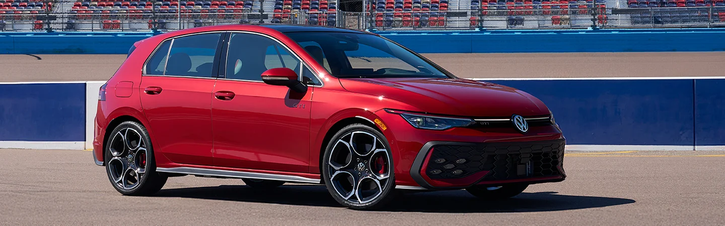 Front side view of a red 2025 Volkswagen Golf GTI parked on a race track