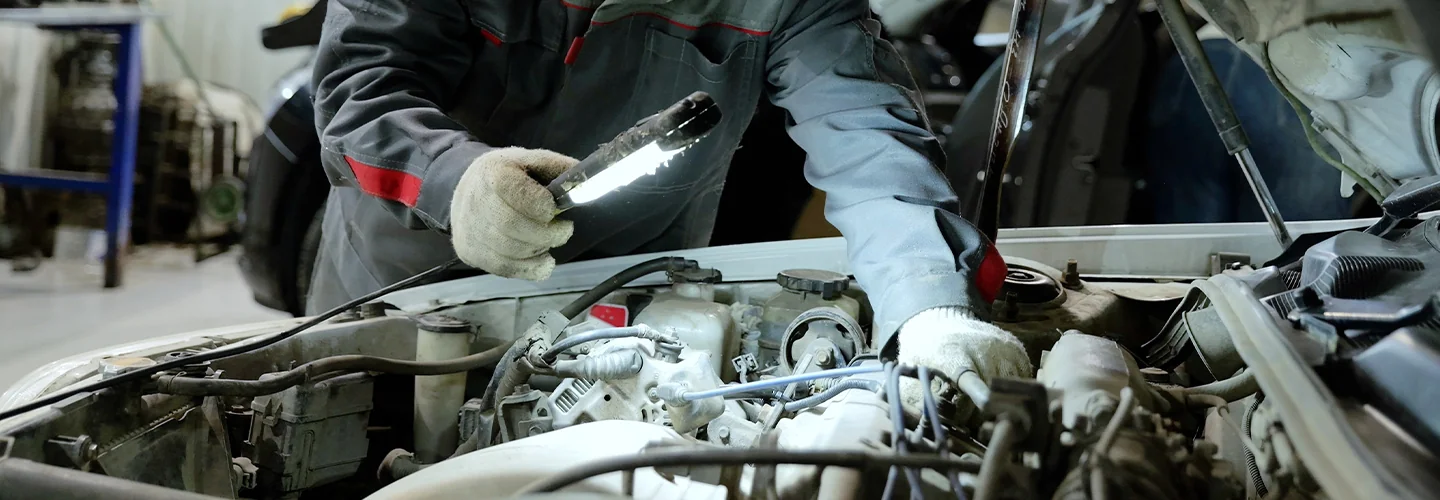 auto mechanic hlding a flashlight looking in engine