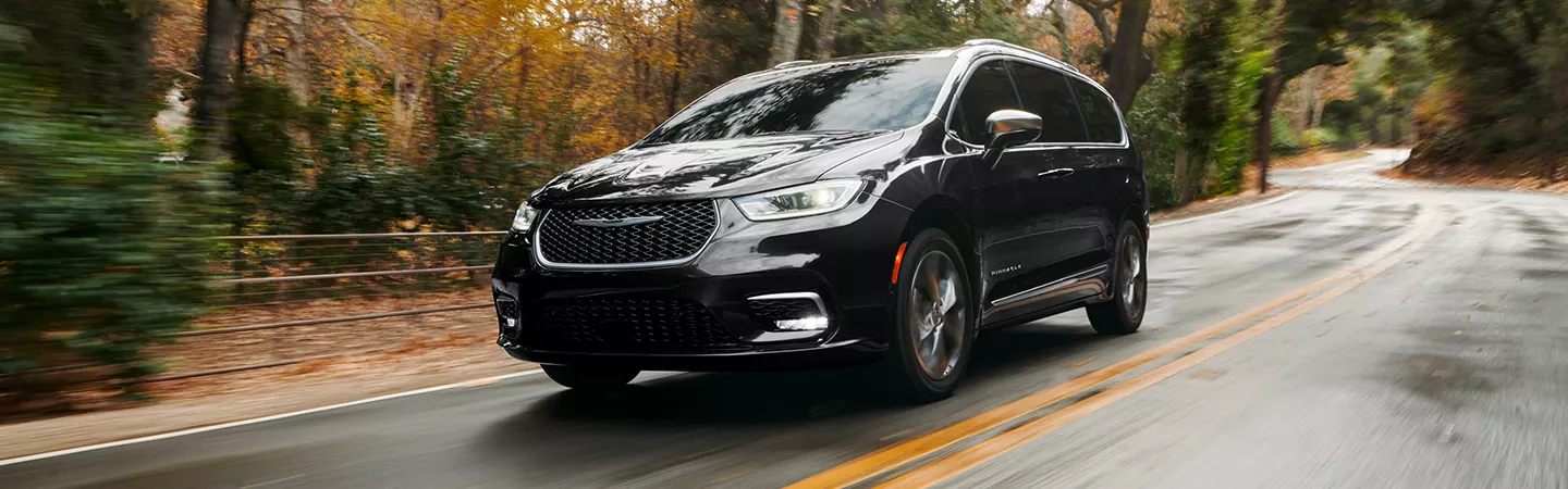 Front view of the 2026 Chrysler Pacifica driving on a wooded road in autumn