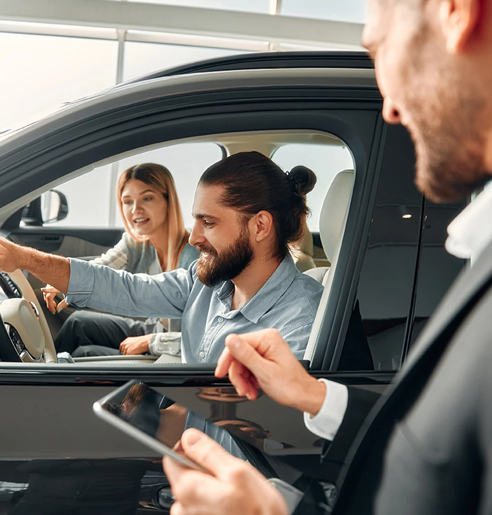 couple in a car with salesperson outside explaining features