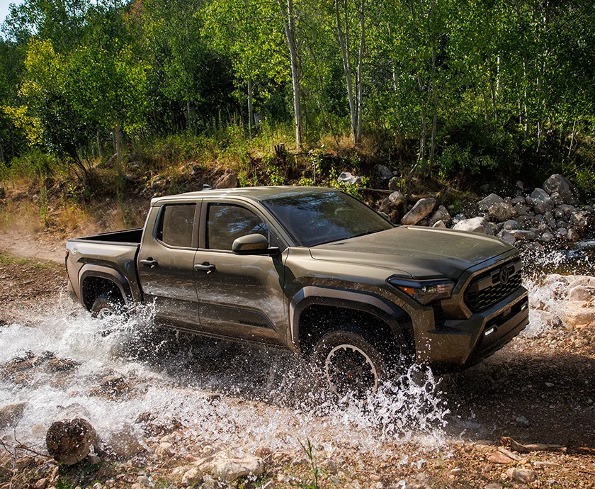 Side view of a green 2026 Toyota Tacoma driving though a river