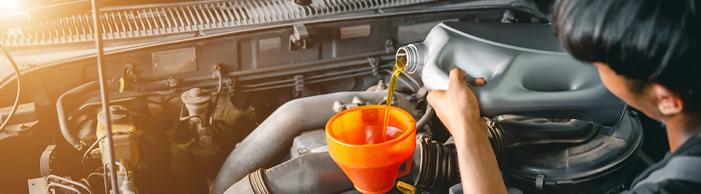 auto mechanic pouring oii in engine