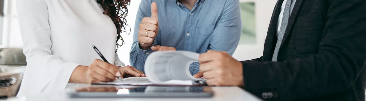 Three people standing while one signs a document and another is holding a thumbs up