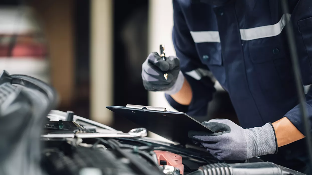 Mechanic taking notes on a clipboard while looking under the hood of a car