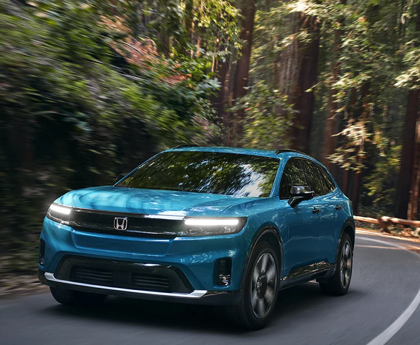 Front view of a blue 2026 Honda Prologue driving on a wooded road
