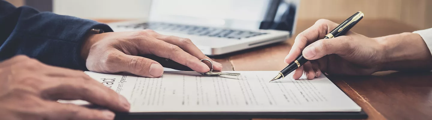 Person signing a document with someone handing them keys