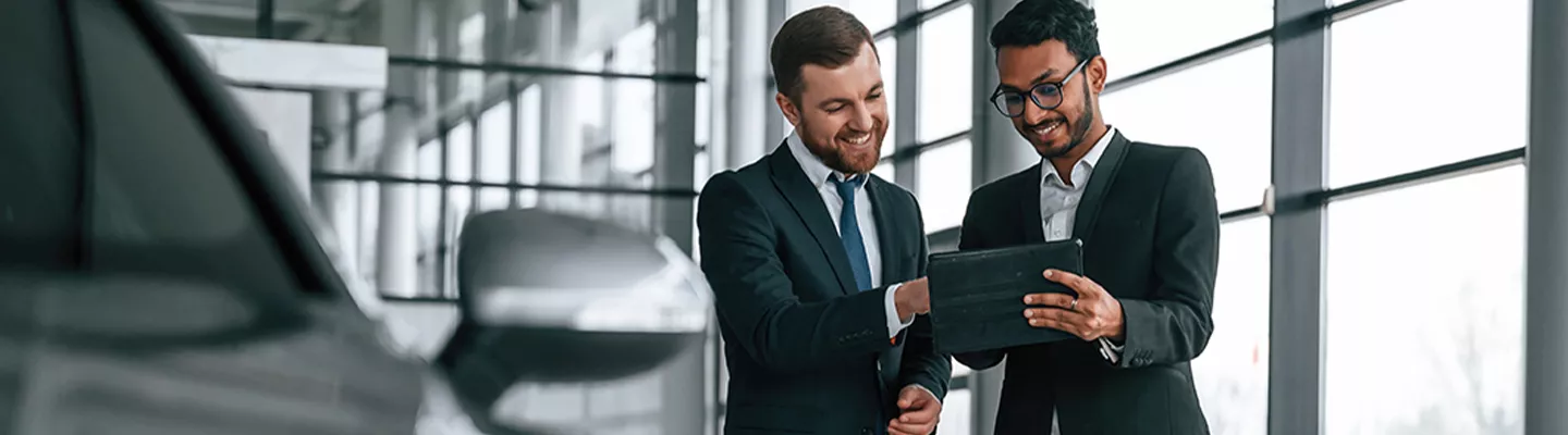 Two people looking at a tablet next to a new Volkswagen