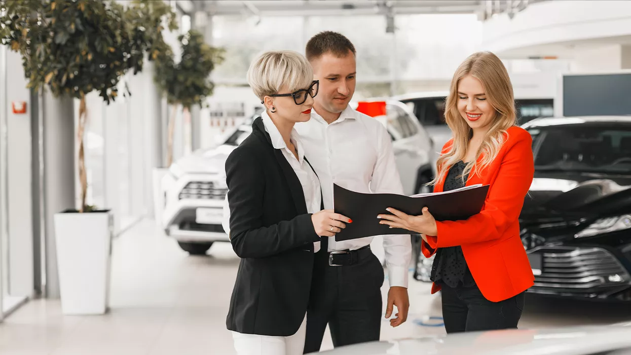 Three people looking at a paper together in a car dealership