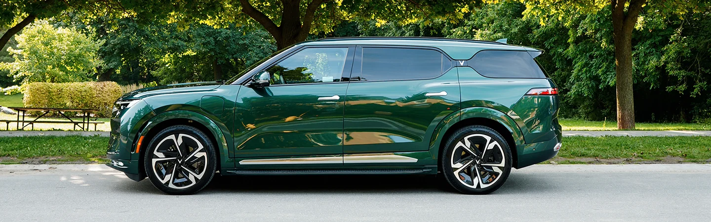 Side view of a parked green 2025 VinFast VF 9 next to a park