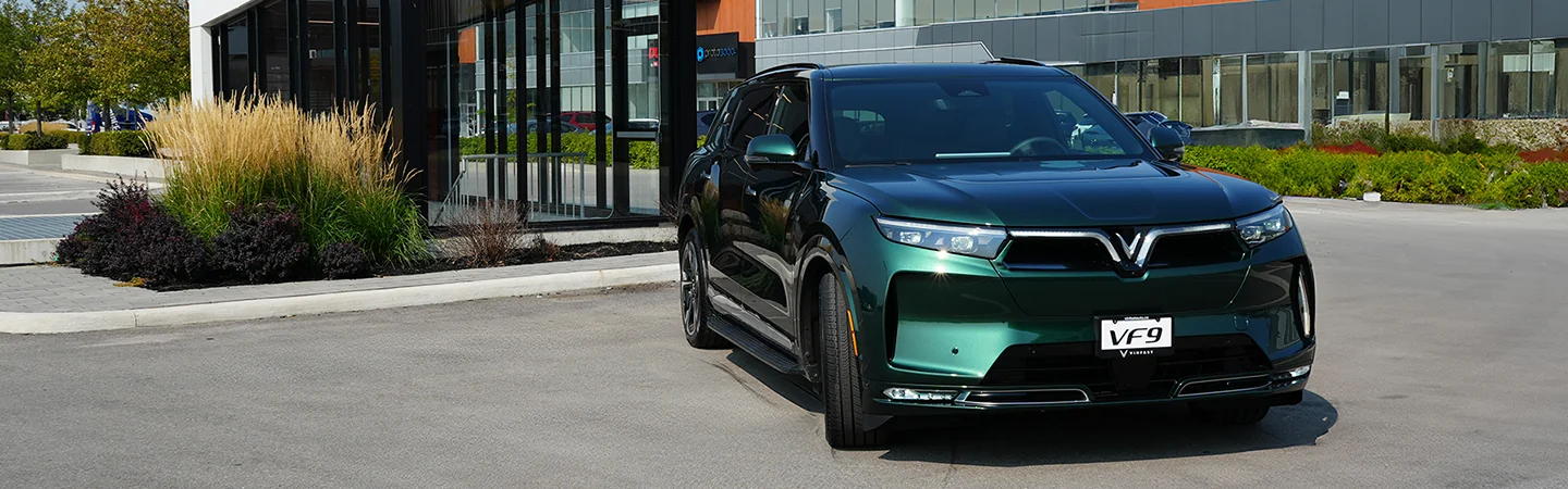 Front view of a green 2025 VinFast VF 9 driving away from a building