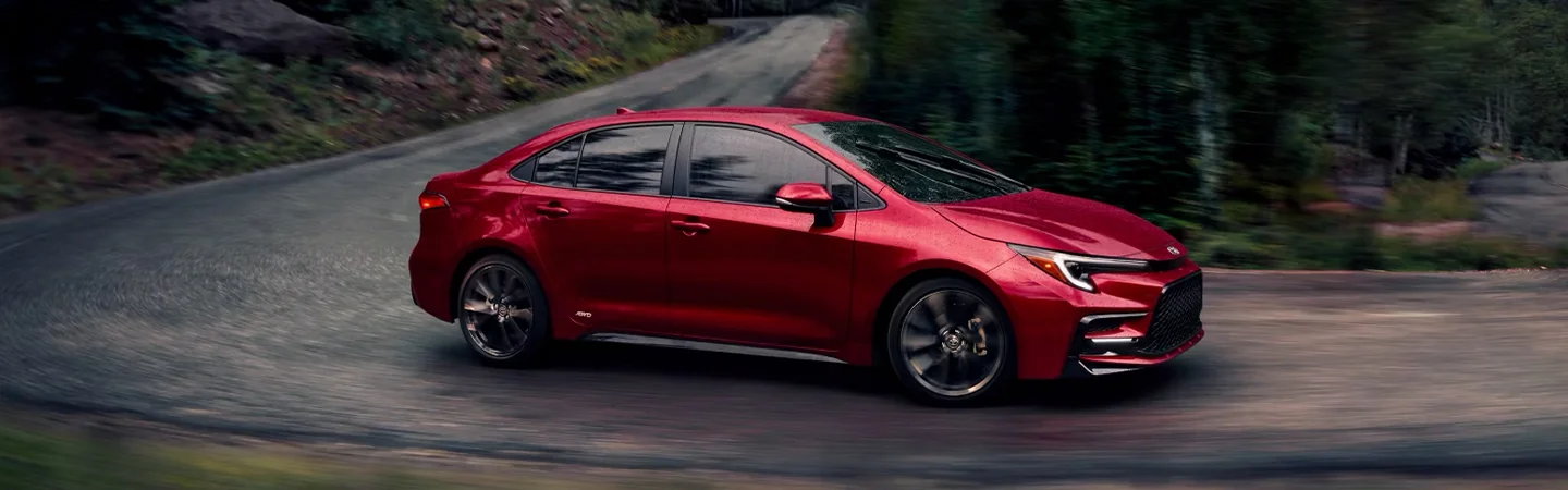 Side view of a red 2024 Toyota Corolla driving down the road in the woods