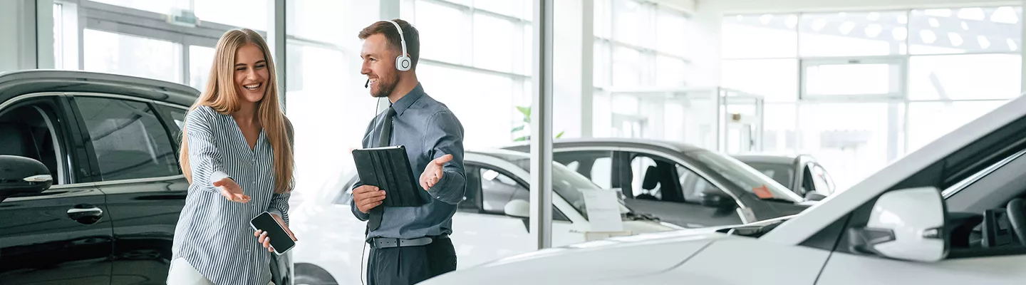 salesman with a tablet and headset on showing a customer a vehicle