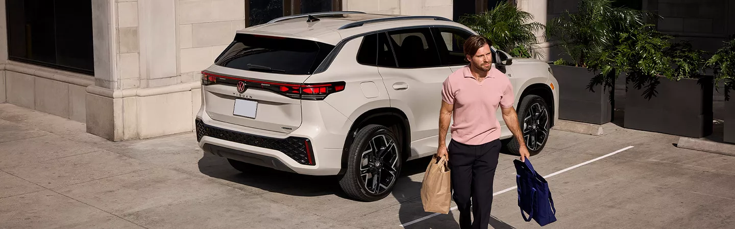 2025 Volkswagen Tiguan parked in a parking space with someone walking away from it holding shopping bags