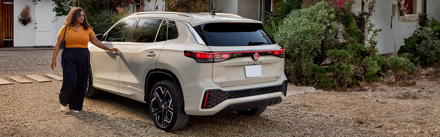Person walking toward a 2025 Volkswagen Tiguan parked in front of a home