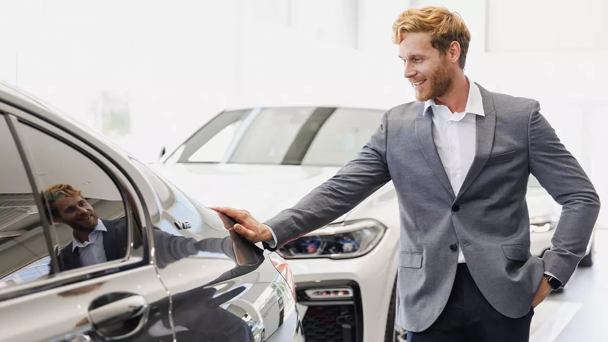 A man in a suit examines a car, showcasing a thoughtful expression as he assesses its features.