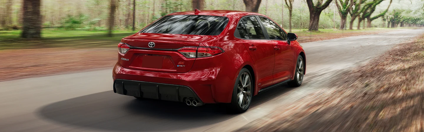 Back view of a red 2026 Toyota Corolla driving on a wooded road