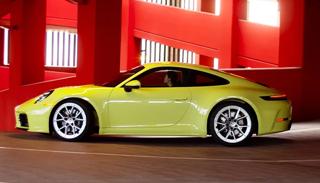 Side view of a yellow 911 Carrera driving in a parking garage