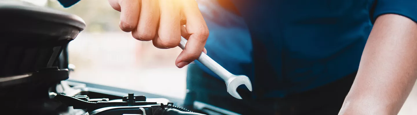 mechanic holding a wrench working on a vehicle under the hood