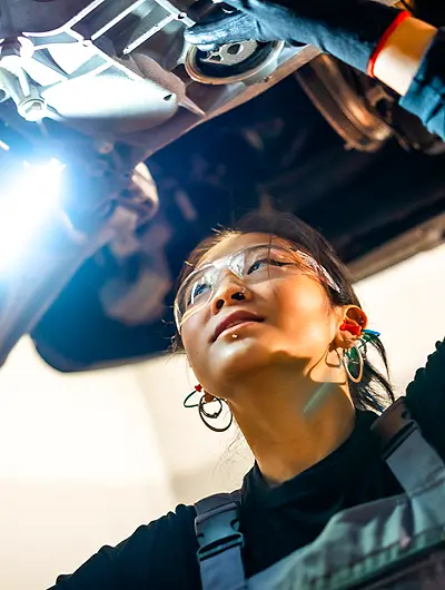 mechanic in the shop standing under a vehicle with mechanic light