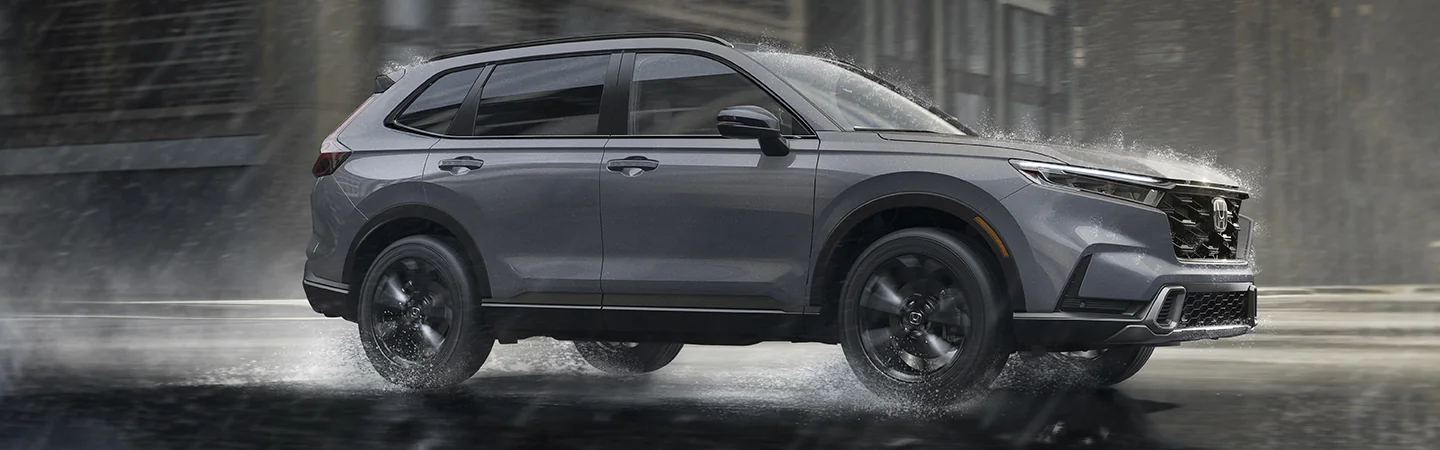 Side view of a gray 2026 Honda CR-V Hybrid driving in the rain in the city