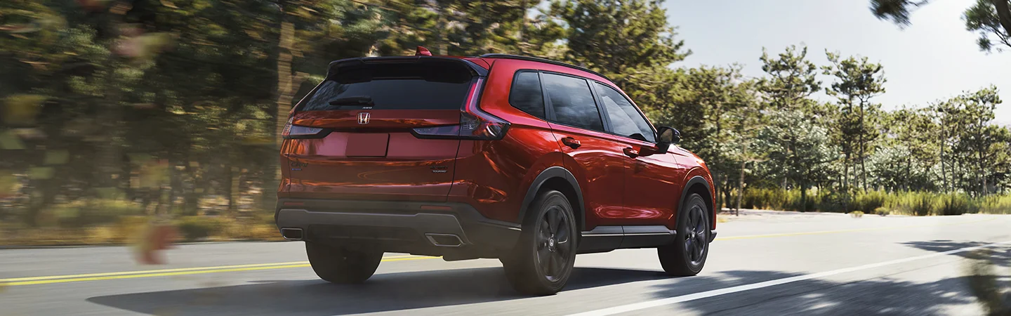 Back view of a red 2026 Honda CR-V Hybrid driving on a wooded road