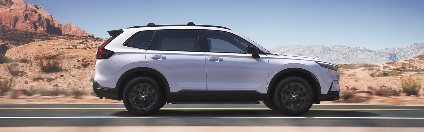 Side view of a white 2026 Honda CR-V Hybrid driving in the desert