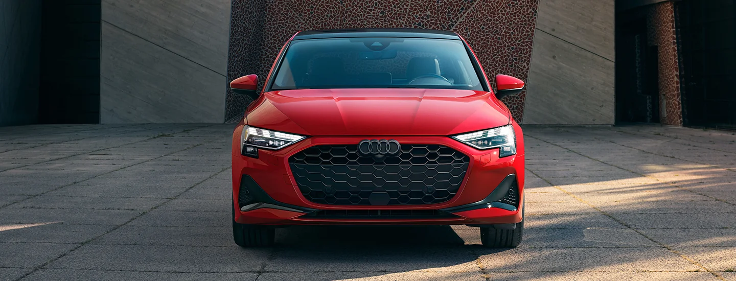 Front view of a parked red 2025 Audi A3 in front of a building