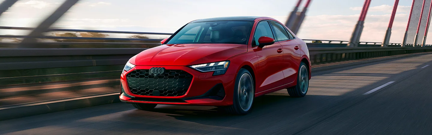 Front view of a red 2025 Audi A3 driving over a bridge