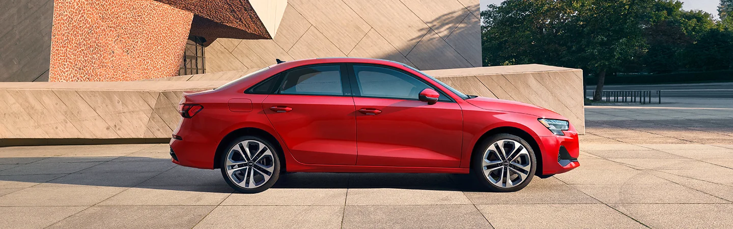 Side view of a parked red 2025 Audi A3 next to a building