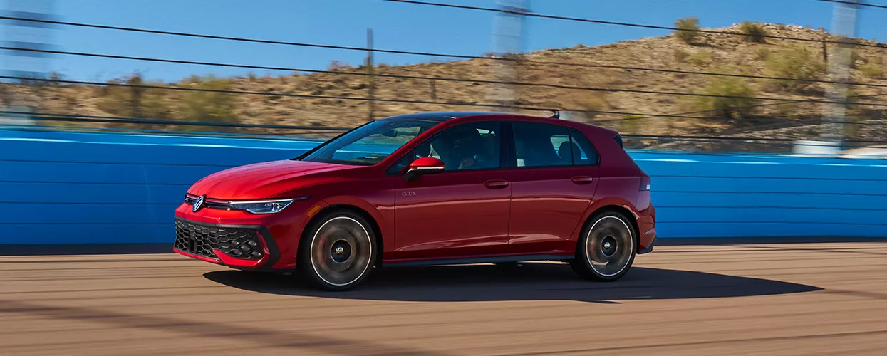 Side view of a red Volkswagen Golf GTI driving on a road next to some water
