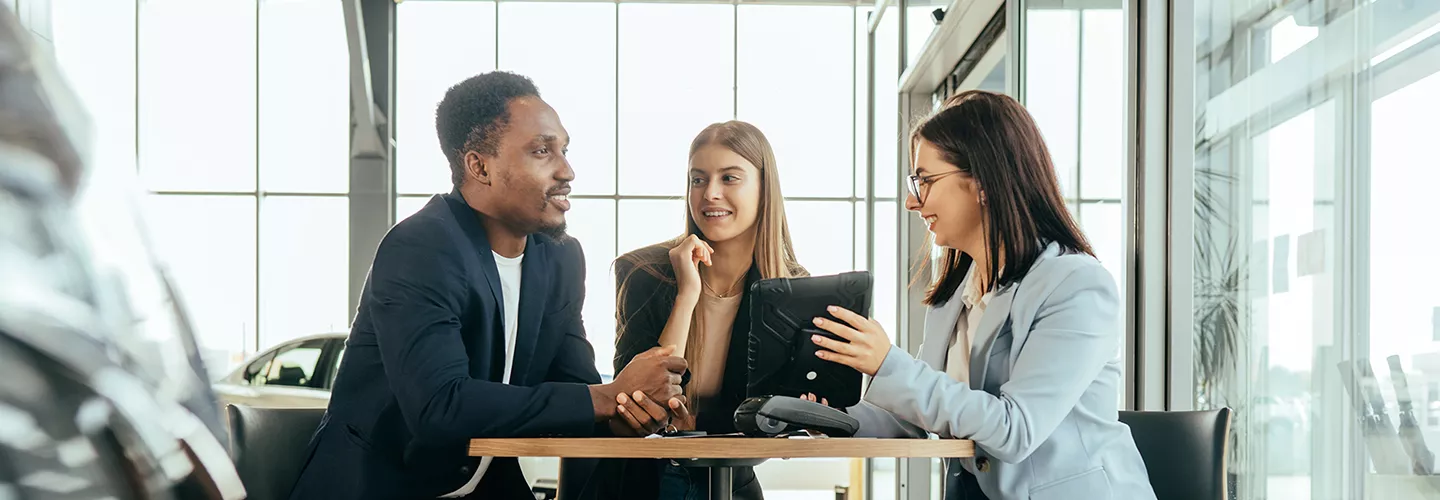 saleswoman going over documents on a tablet with a husband and wife in the dealership