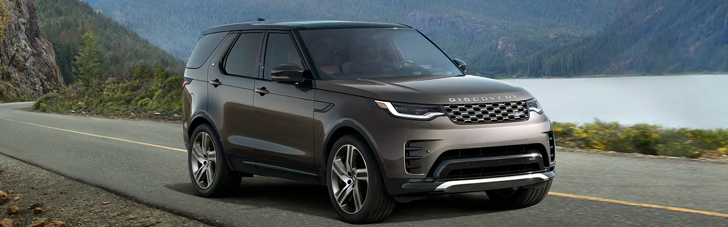 Gray 2025 Discovery driving on a road by a lake