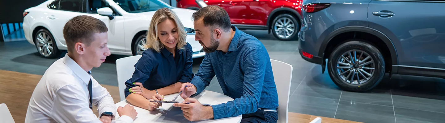 Three people sitting at a car dealership talking about a contract