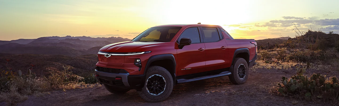 A red 2025 Chevrolet Silverado EV parked with mountains in the background