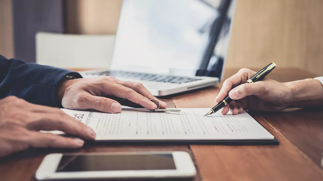 Person signing document and someone sliding car keys across the table