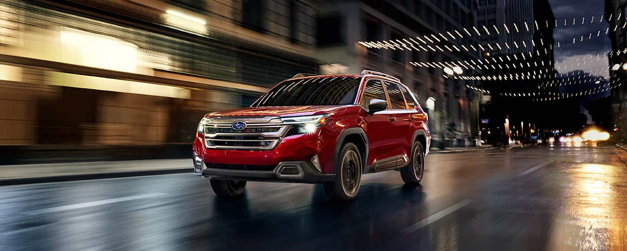 a bright red 2026 Subaru Forester drinv at night downtown in city