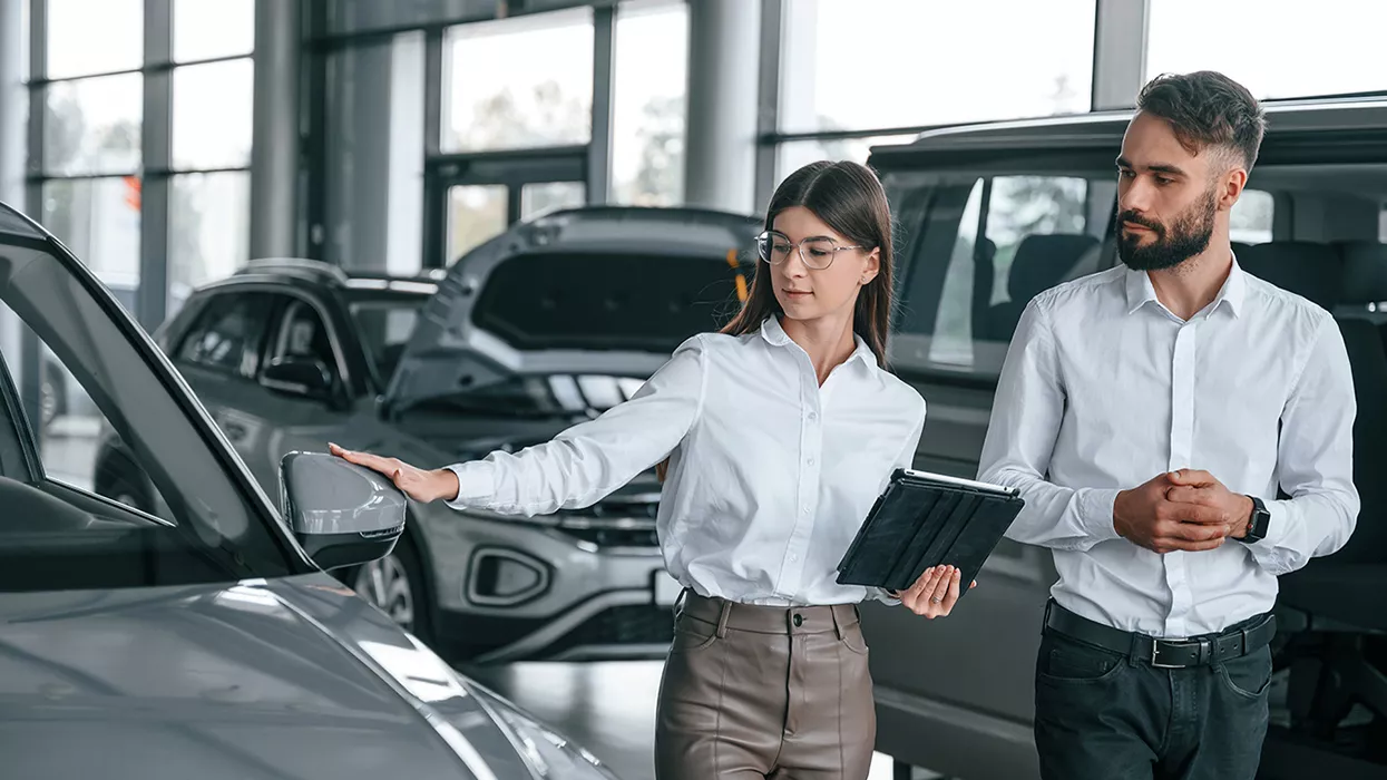 Two people walking and looking at cars in a dealership, one of them is holding a tablet