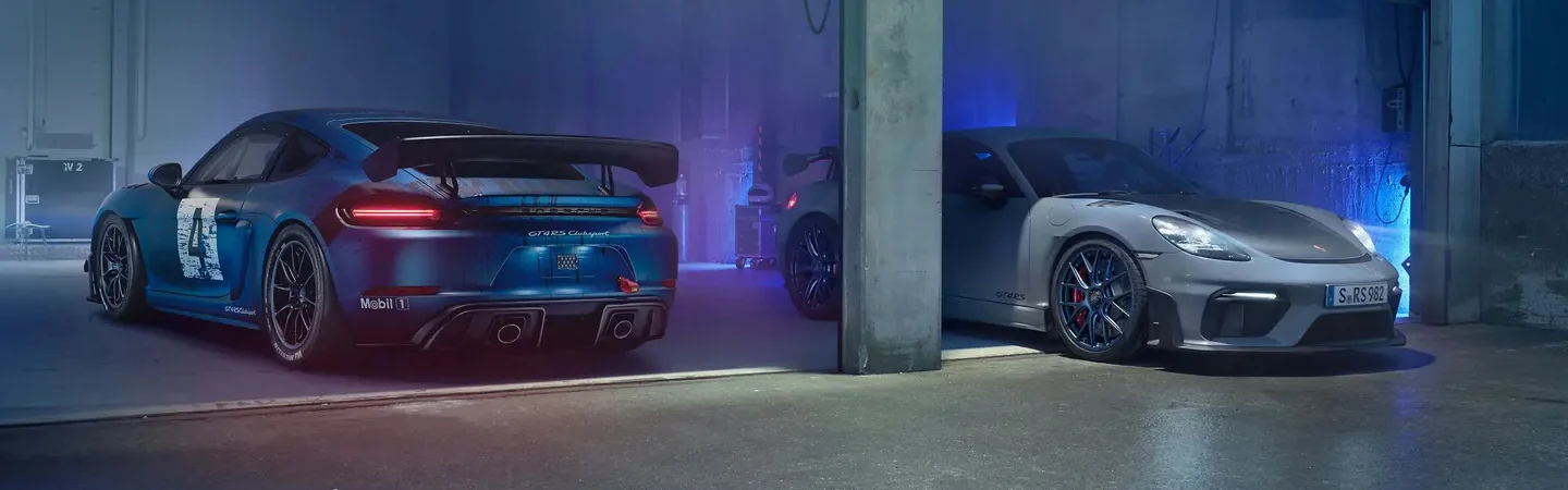 Two 2024 Porsche Cayman GT4 parked in a garage a blue and a gray one