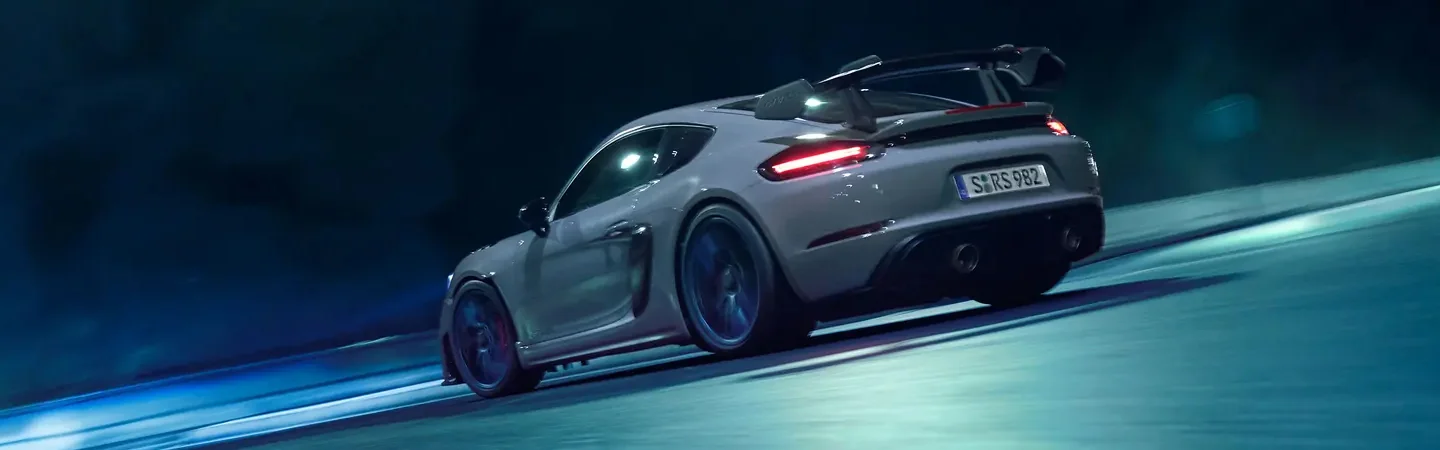 Side view of a gray 2024 Porsche Cayman GT4 driving on a track