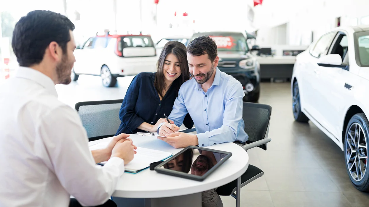 a cuple sitting with car salesperson in showroom going over details of car purchase