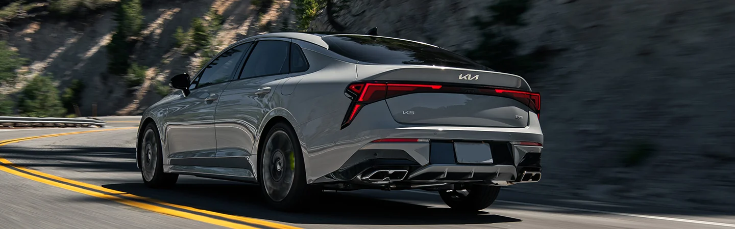 Back view of a gray 2025 Kia K5 driving on a mountain side road