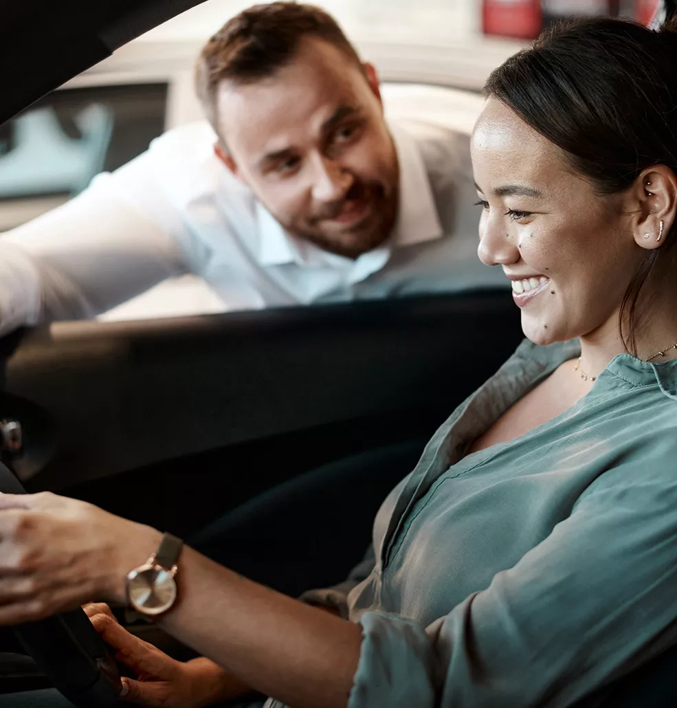 Sales person talking to a customer that is sitting in a new car