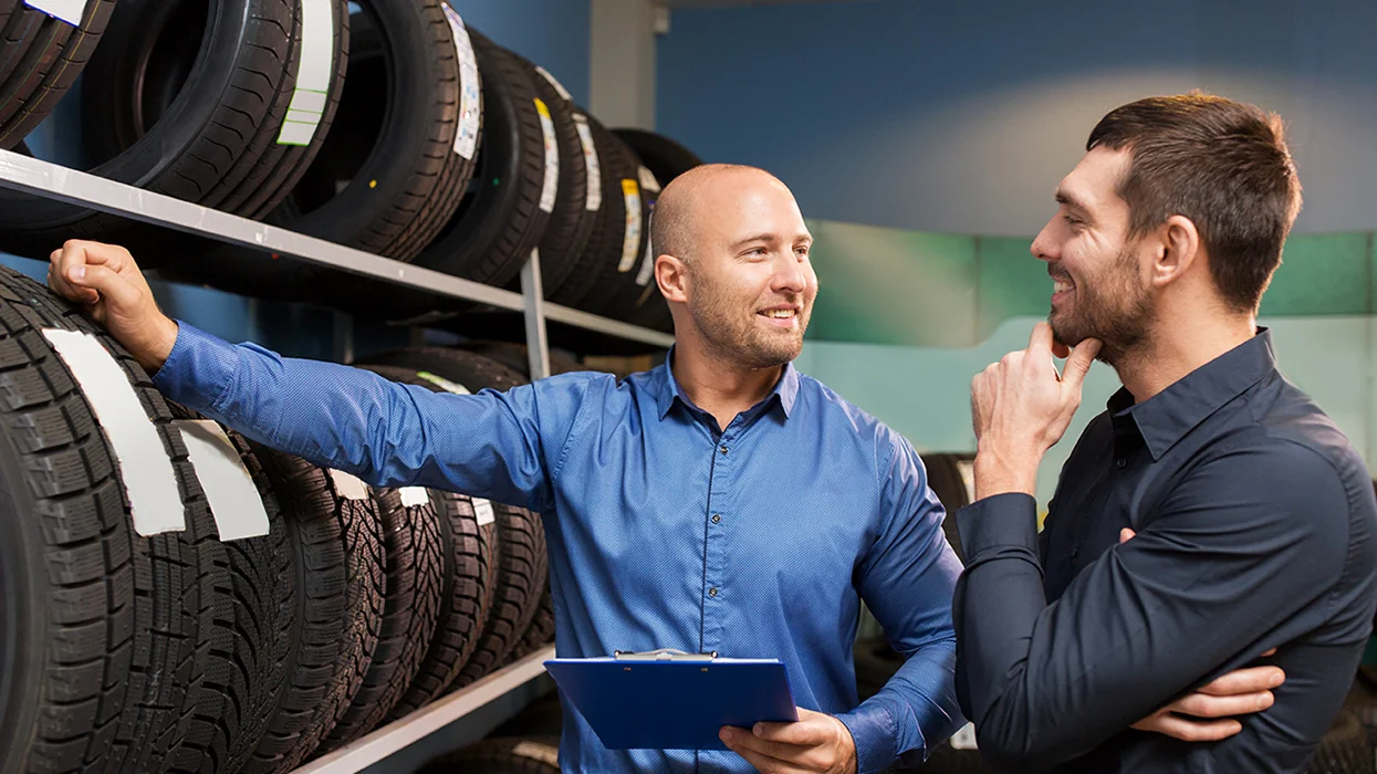 customer with store salesperson going over tire purchase in front of rack of tires in showroom