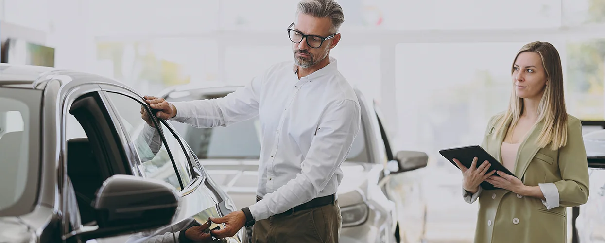 A couple inspects a car at a dealership, engaged in conversation about its specifications and pricing.