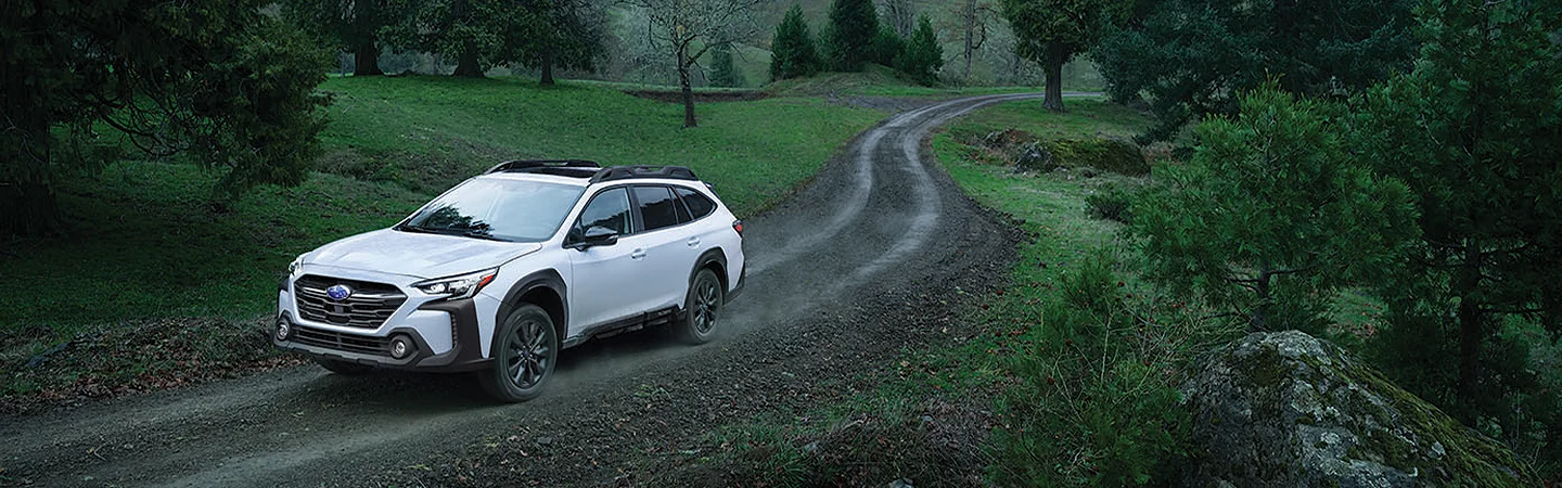 A white 2025 Subaru Outback driving on a dirt road in a forest in Nederland, TX