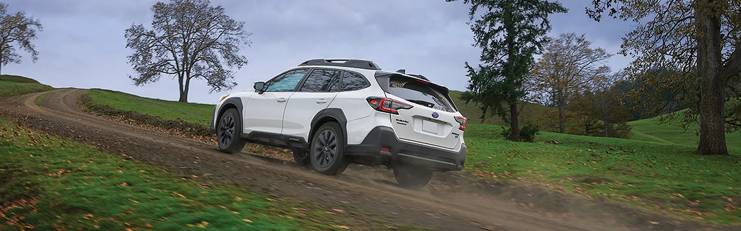 Back side view of a white 2025 Subaru Outback driving on a dirt road in Nederland, TX