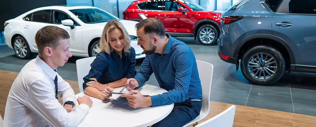 Car salesman talking to two people at a round table about a contract