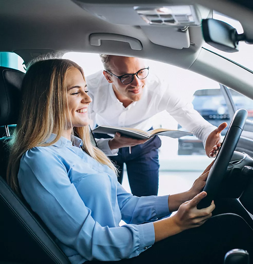 Woman sitting in a car with a salesman standing outside showing her the interior