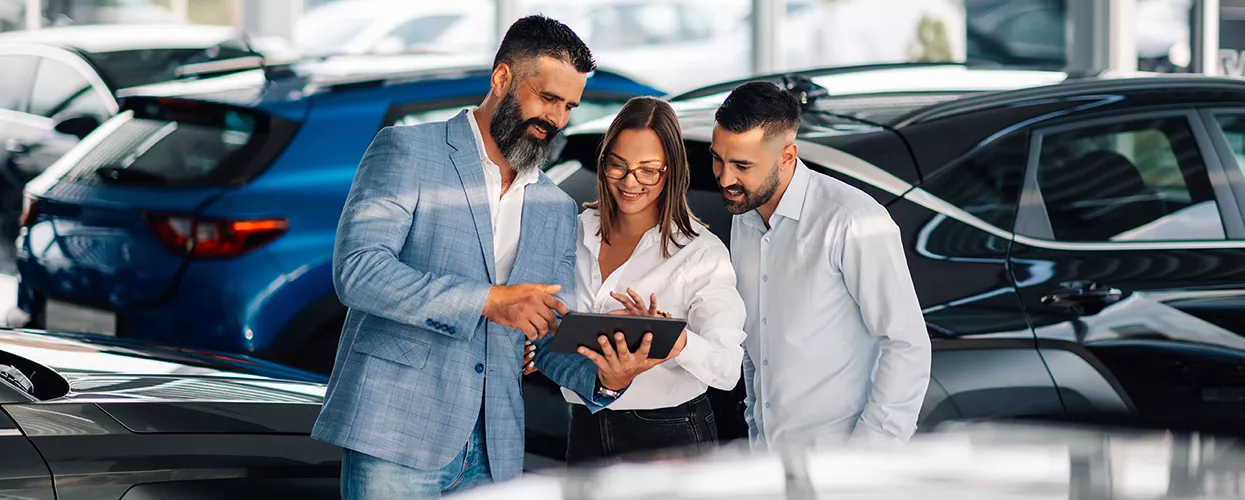 Three people standing around a tablet in a car dealership